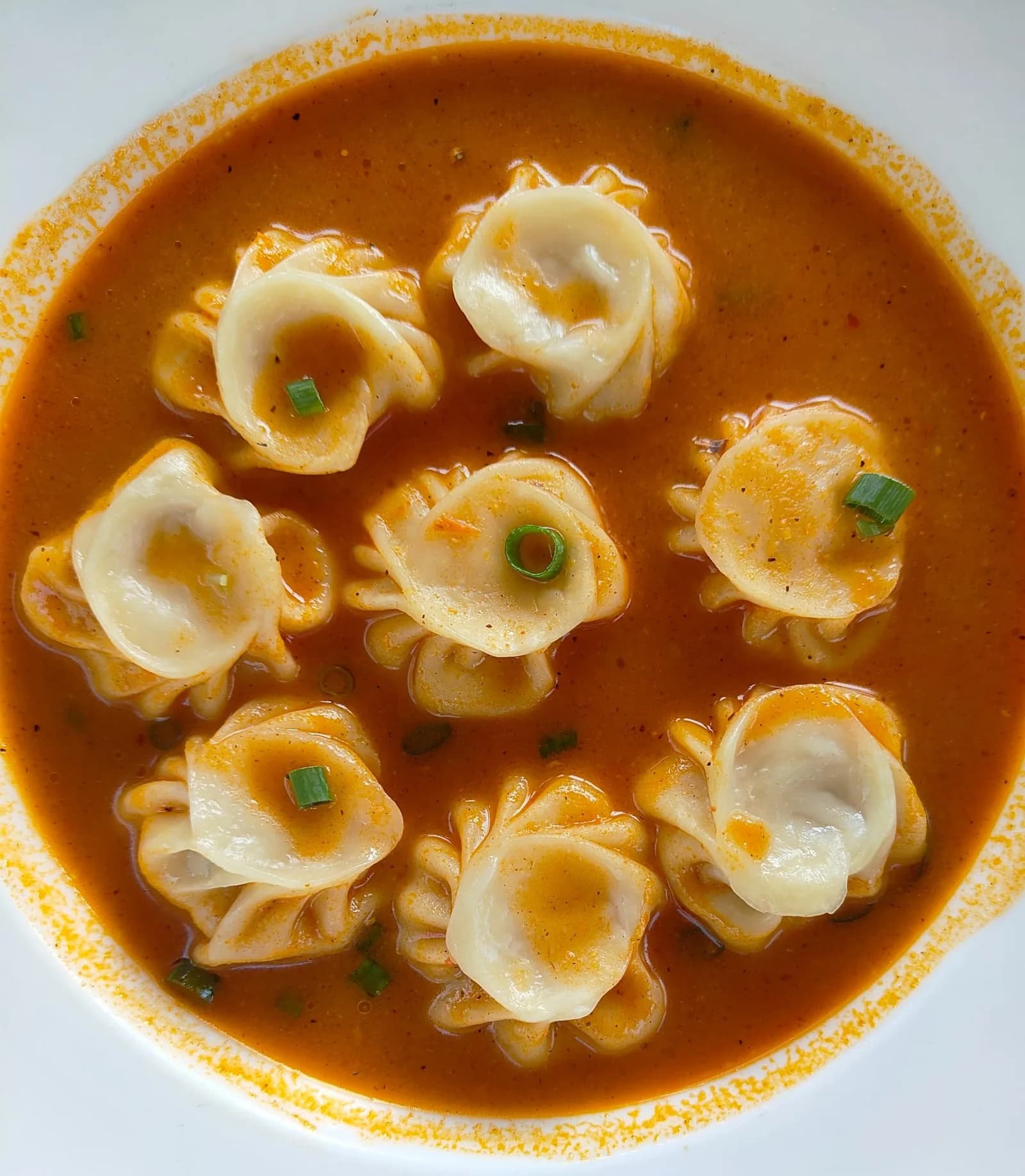 Soup momo in a spicy orange broth garnished with spring onions